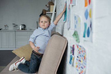 side view of little kid hanging childish pictures on wall at home clipart