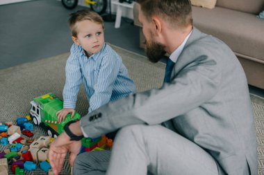 businessman in suit and little son playing with colorful blocks together on floor at home, work and life balance concept clipart