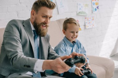businessman and little son playing video games together at home, work and life balance concept clipart