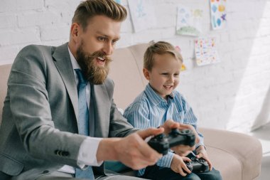 businessman and little son playing video games together at home, work and life balance concept clipart