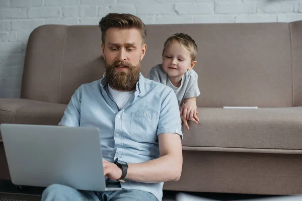 Skäggig Man Använder Laptop Med Son Nära Soffan Hemma — Stockfoto