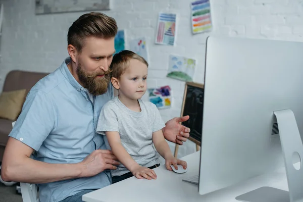 father and little son looking at computer screen while using computer at home