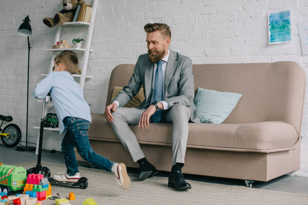 businessman in suit and little son on scooter at home, work and life balance concept