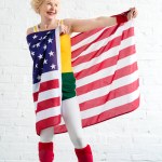 Happy sporty senior woman in sportswear holding us flag and looking away