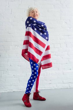 Amerikan bayrağı tutarak ve kameraya gülümseyen vatansever spor giyim mutlu üst düzey sporcumuz görünümünü tam uzunlukta
