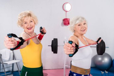sportive senior ladies exercising with resistance bands and smiling at camera clipart