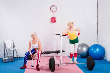 happy sportive senior ladies in sportswear smiling at camera in gym clipart