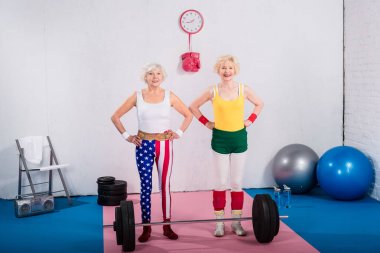 Bel ellerde ile ayakta ve spor salonunda kamera gülümseyen mutlu sportif üst düzey kadın