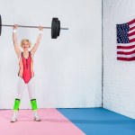 Full length view of sporty senior woman lifting barbell and smiling at camera