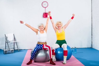 Fitness topları üzerinde oturan ve kameraya gülümseyen mutlu üst düzey sportswomen 