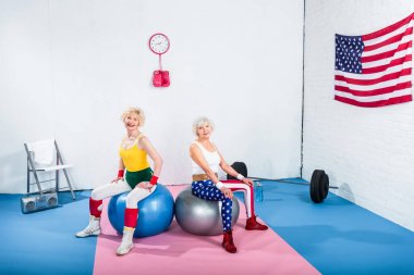 Fitness topları üzerinde oturan ve kameraya gülümseyen mutlu sportif üst düzey kadın
