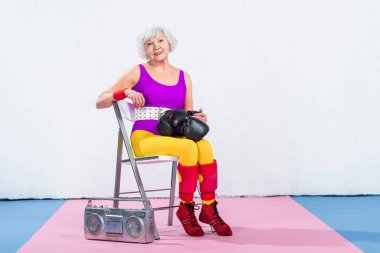 kadın boks eldivenli oturan ve kameraya gülümseyen kıdemli mutlu sportif 