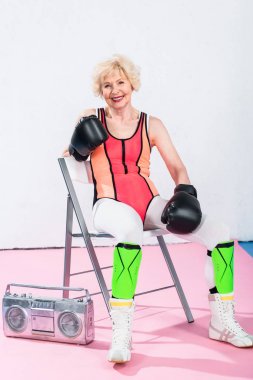 Sportif boks eldiven kayıt cihazı ile oturma ve kameraya gülümseyen kadın kıdemli