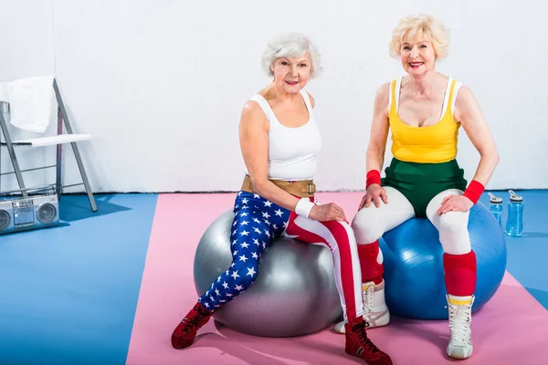 Sportliche Seniorinnen Sportbekleidung Sitzen Auf Fitnessbällen Und Lächeln Die Kamera — Stockfoto