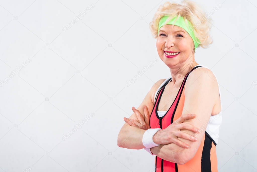 portrait of beautiful happy sporty senior woman standing with crossed arms isolated on grey