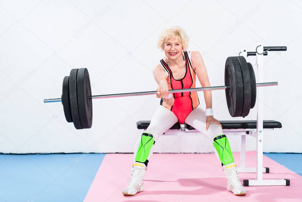 happy senior sportswoman lifting barbell and smiling at camera