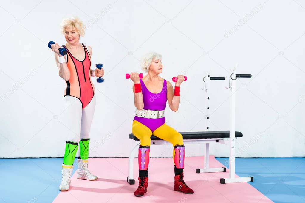 sporty senior women in sportswear exercising with dumbbells in gym