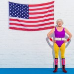 Happy senior woman standing with hands on waist near us flag and smiling at camera