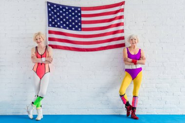 Amerikan bayrağı yakınındaki çapraz kollar ile ayakta ve kameraya gülümseyen güzel üst düzey sportswomen 