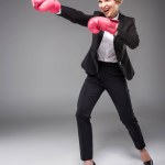 Возбужденные деловая женщина в костюме и розовые боксерские перчатки, изолированные на серый