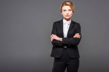 serious businesswoman posing in suit with crossed arms, isolated on grey clipart