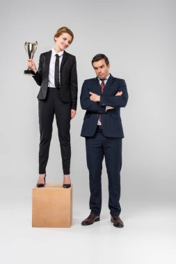 happy businesswoman with trophy cup standing on podium, upset businessman standing near, isolated on grey clipart