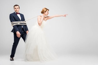 bride pointing and pulling groom bound with rope, isolated on grey, feminism concept clipart