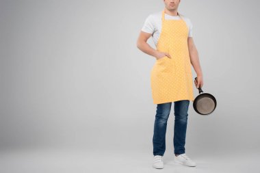 cropped view of male householder in yellow apron holding frying pan, isolated on grey clipart
