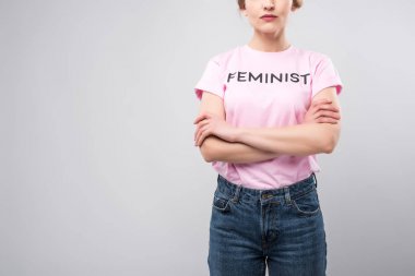 cropped view of woman in pink feminist t-shirt posing with crossed arms, isolated on grey clipart