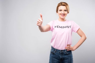 smiling woman in pink feminist t-shirt showing thumb up, isolated on grey clipart