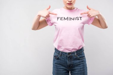 cropped view of woman pointing at pink feminist t-shirt, isolated on grey clipart
