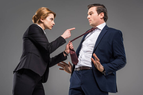 angry female boss pointing at businessman in formal wear, isolated on grey