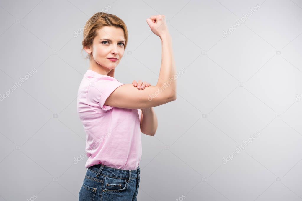 feminist woman in pink t-shirt showing muscles, isolated on grey