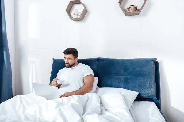 Hombre trabajando en el ordenador portátil en la cama - foto de stock