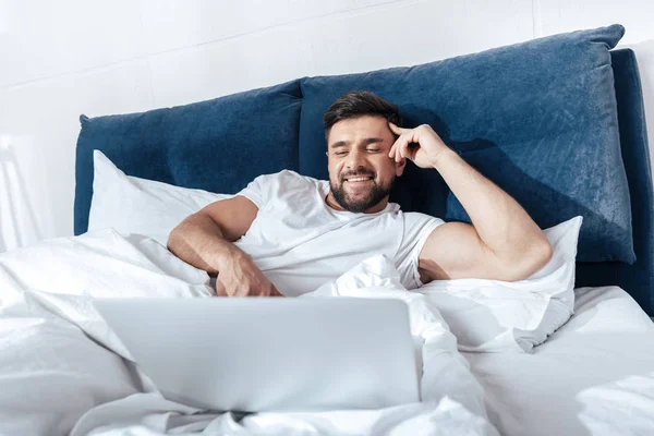 Uomo utilizzando il computer portatile a letto — Foto stock