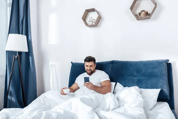 Homem jovem usando Smartphone na cama — Fotografia de Stock