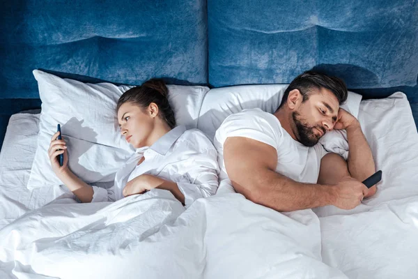 Pareja usando teléfonos inteligentes en la cama - foto de stock