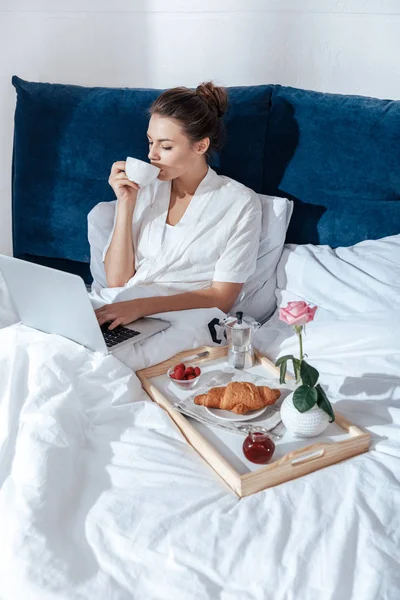 Mujer joven usando portátil en la cama - foto de stock