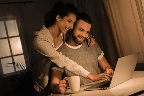 Couple souriant utilisant un ordinateur portable à la maison — Photo de stock