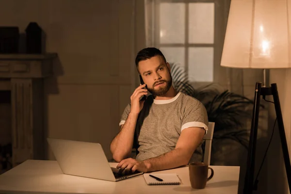 Hombre hablando en el teléfono inteligente mientras trabaja en el ordenador portátil - foto de stock