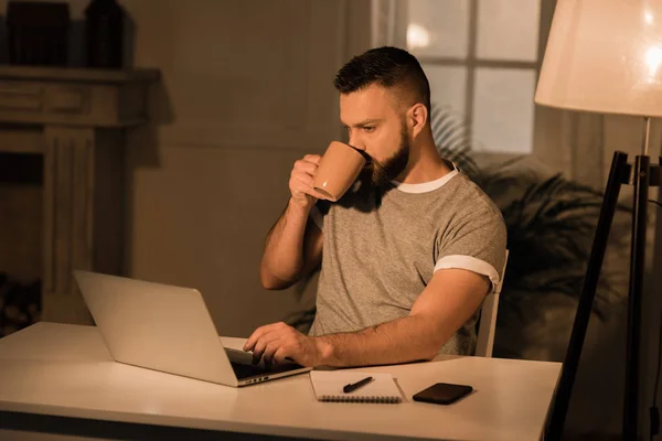 Mann trinkt Kaffee während er am Laptop arbeitet — Stockfoto