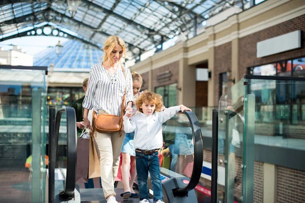Madre con niños levantándose en escaleras mecánicas en el centro comercial - foto de stock