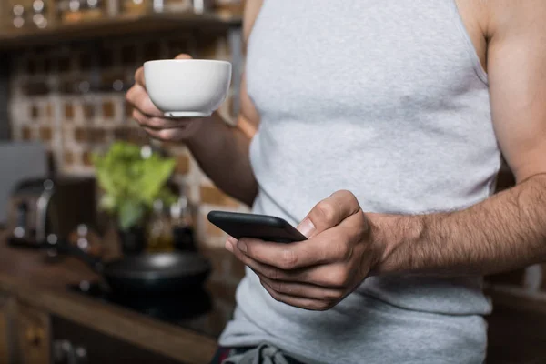 Человек с помощью смартфона во время питья кофе — стоковое фото