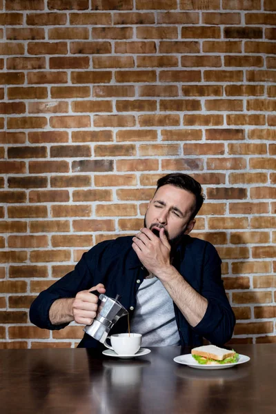 Young man drinking coffee and yawning — Stock Photo