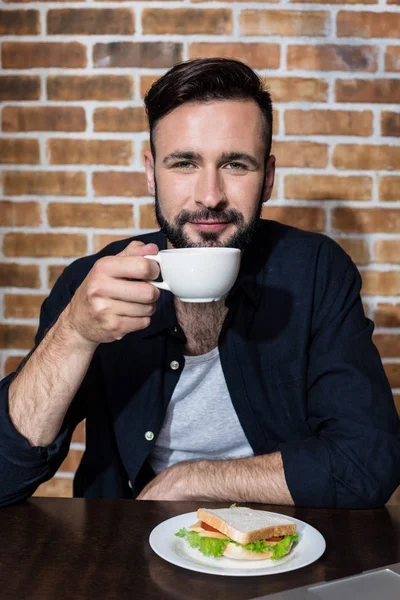 Homem bebendo café com sanduíche — Fotografia de Stock