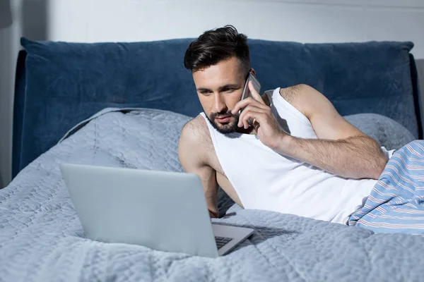 Junger Mann benutzt Gadgets im Bett — Stockfoto