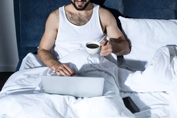 Young man using laptop in bed — Stock Photo