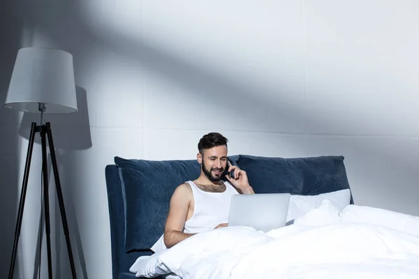 Schöner Mann mit Gadgets im Bett — Stockfoto