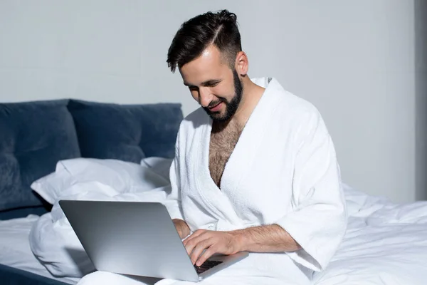 Bonito homem usando laptop na cama — Fotografia de Stock