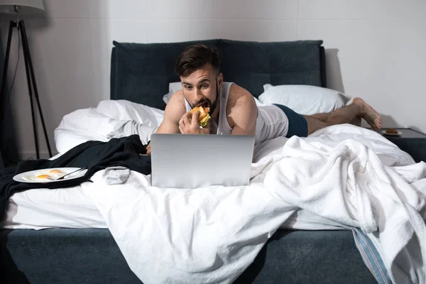 Young man using laptop in bed — Stock Photo